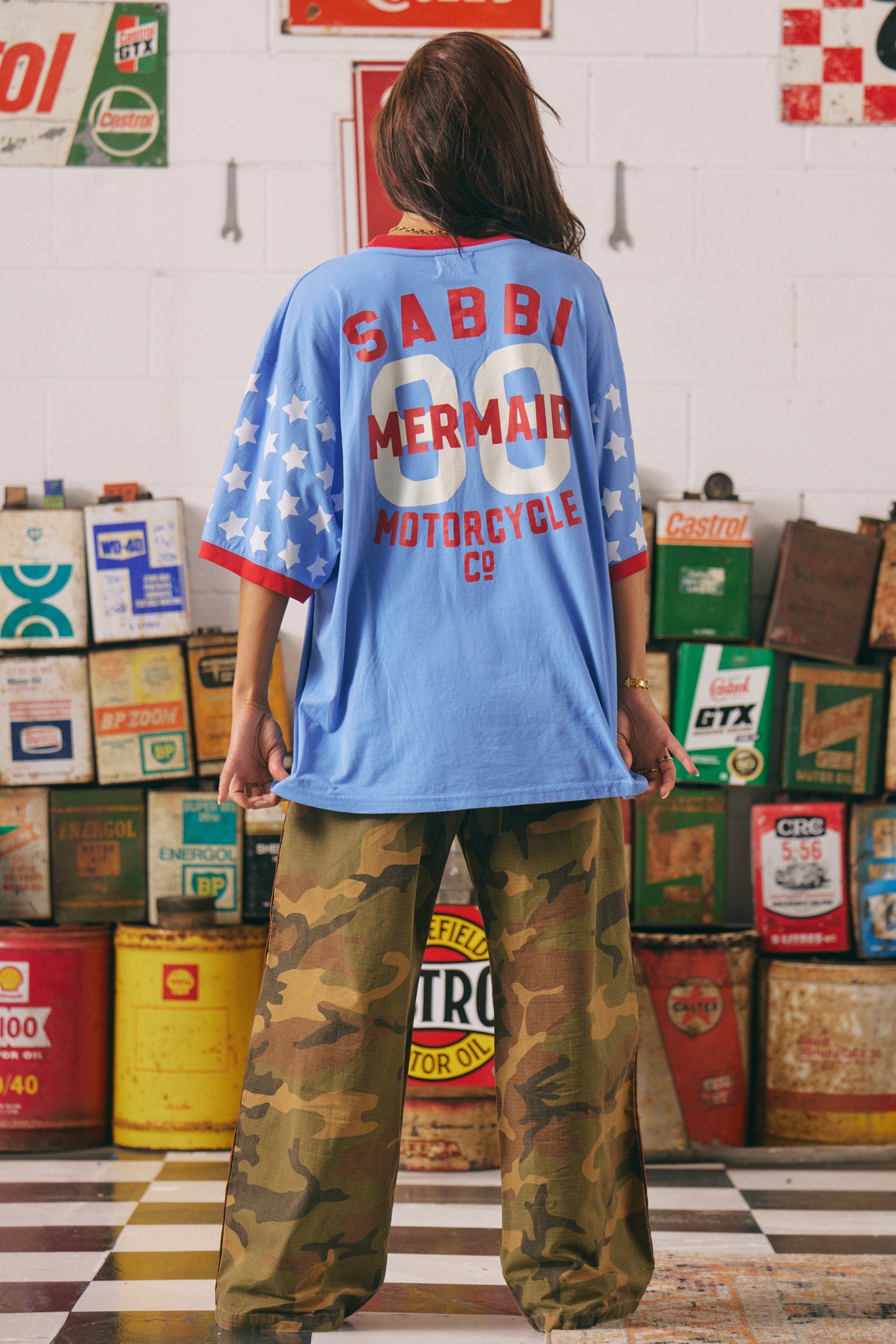 Born to stand out. The Dream Big Brenda Tee in Periwinkle is a fearless blend of retro biker energy and bold feminine power. Featuring the iconic winged mermaid front print and bold varsity-inspired back graphic, this oversized tee is made for wild hearts who ride loud and dream louder.
Designed in a vibrant periwinkle blue with contrast red ribbed trims and all-over star-print sleeves, it’s a punch of colour, confidence, and comfort in one seriously cool silhouette.