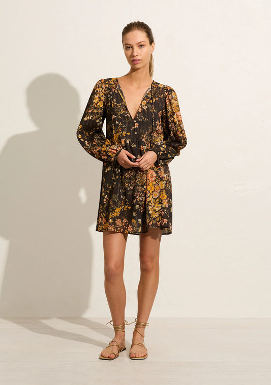 The Callie Agnes Mini Dress is crafted from cotton with a gold lurex thread against a dark-based floral. This style boasts a V neckline with an optional tie closure, long voluminous sleeves into a half-fixed, half-elasticated cuff and specialty gold buttons.