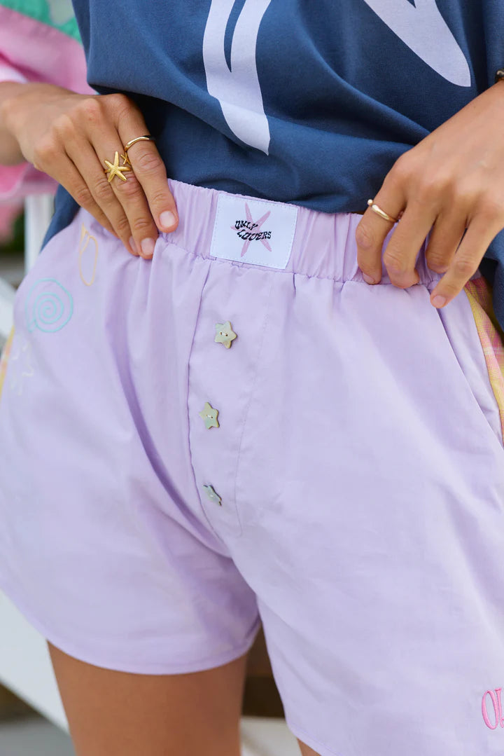 The Shell Club Boxer Short is a bold take on summer nostalgia… easy to wear, instantly fun, and full of thoughtful detail. Crafted from 100% washed cotton, they’re lightweight, durable, and made for endless warm-weather days. Contrast tartan panels run down each side, Mother of Pearl star buttons shimmer at the front, and subtle shell embroidery traces the pocket, a little nod to collecting seaside treasures along the way. 