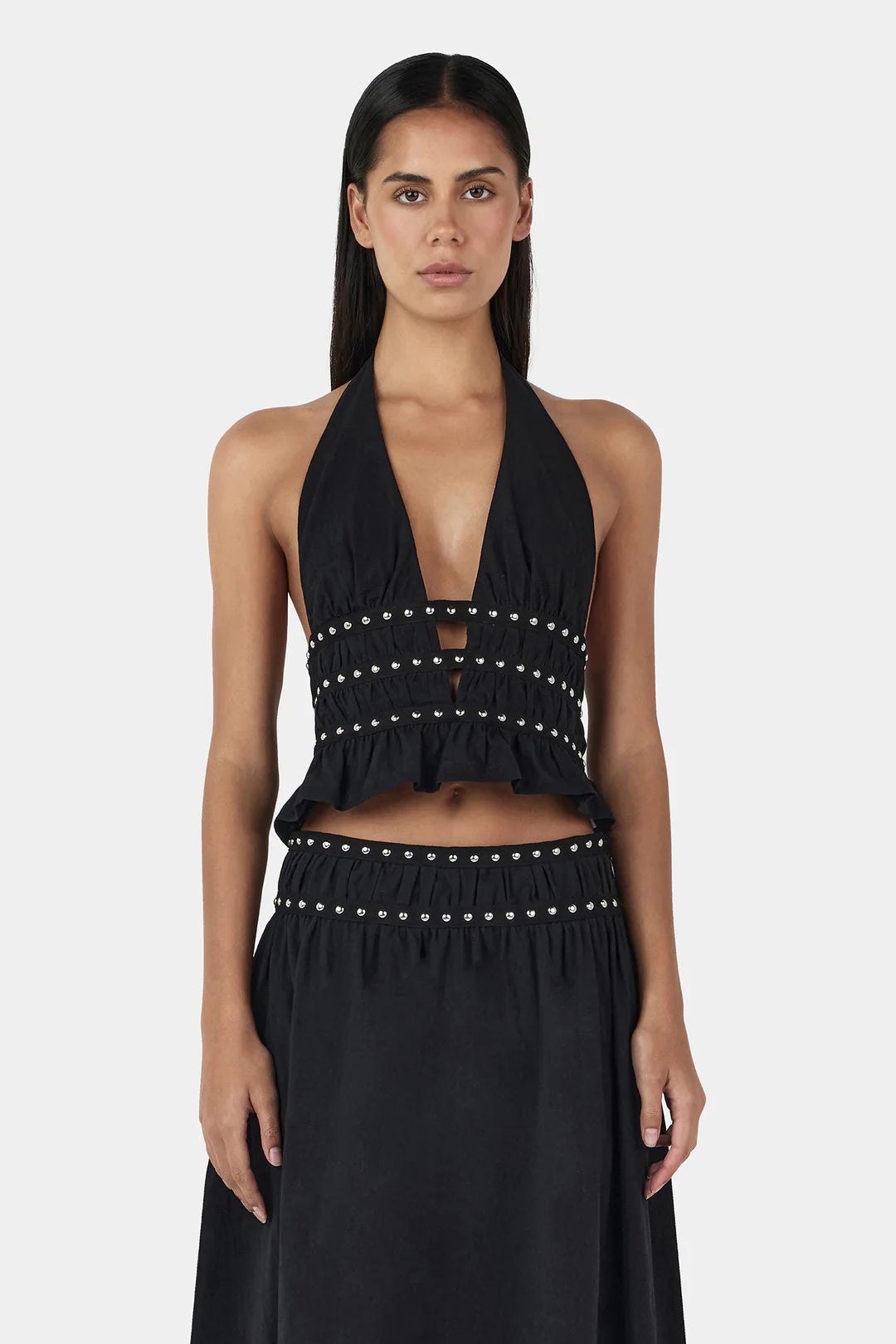 The Mavis Studded Top is a halter-style piece featuring an elasticated neckline, adjustable back ties, and a gathered bust for a flattering silhouette. A plunging neckline and silver studs along the bodice add an elevated detail. Pair with the matching Tabby Studded Midi Skirt for a complete look.