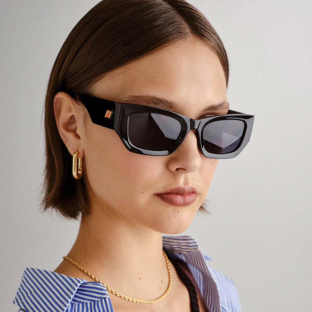 Timelessly elegant and sophisticated, our BEACHCOMBER sunglasses are an everyday staple. Featuring a low bridge fit, bold edges and bevelled lines, this frame is finished with a square flagstripe hardware with custom enamel fill to each temple.
• Finished in shiny black with bright gold hardware and dark tonal lenses for a sleek look.
• Made using BPA free polymer plastic which is lightweight, durable and impact resistant
• Fitted with shatterproof and scratch resistant polycarbonate lenses.