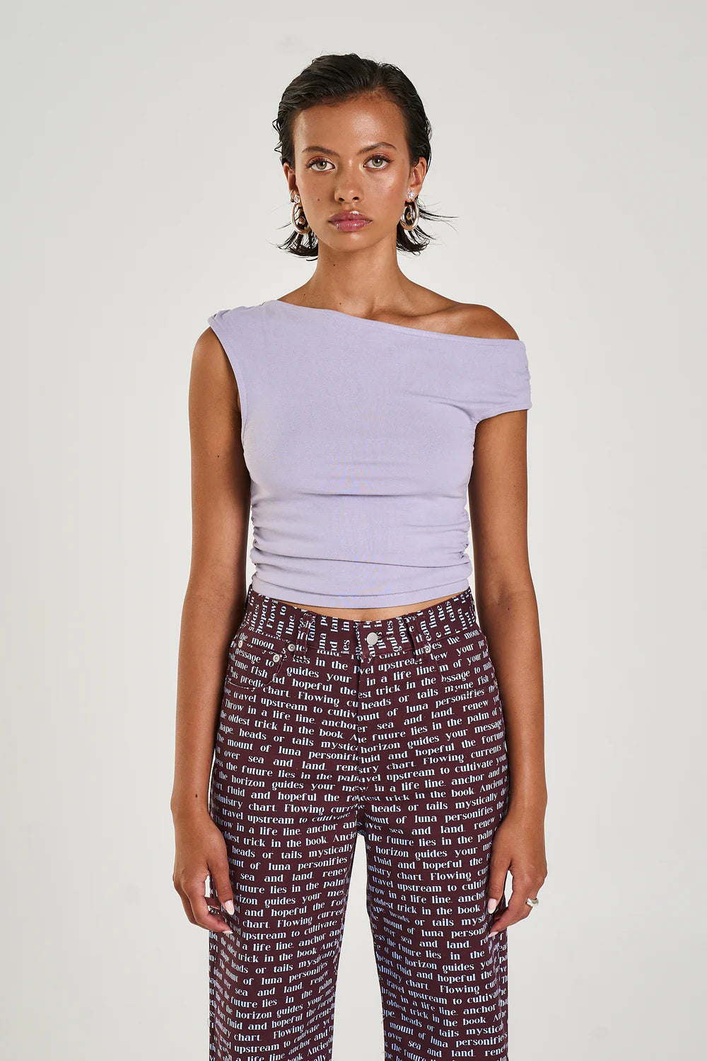 The Off Shoulder Tank in a seafoam lilac hue has been constructed from a stretchy cotton blend, featuring a ruched midsection for a flattering fit.