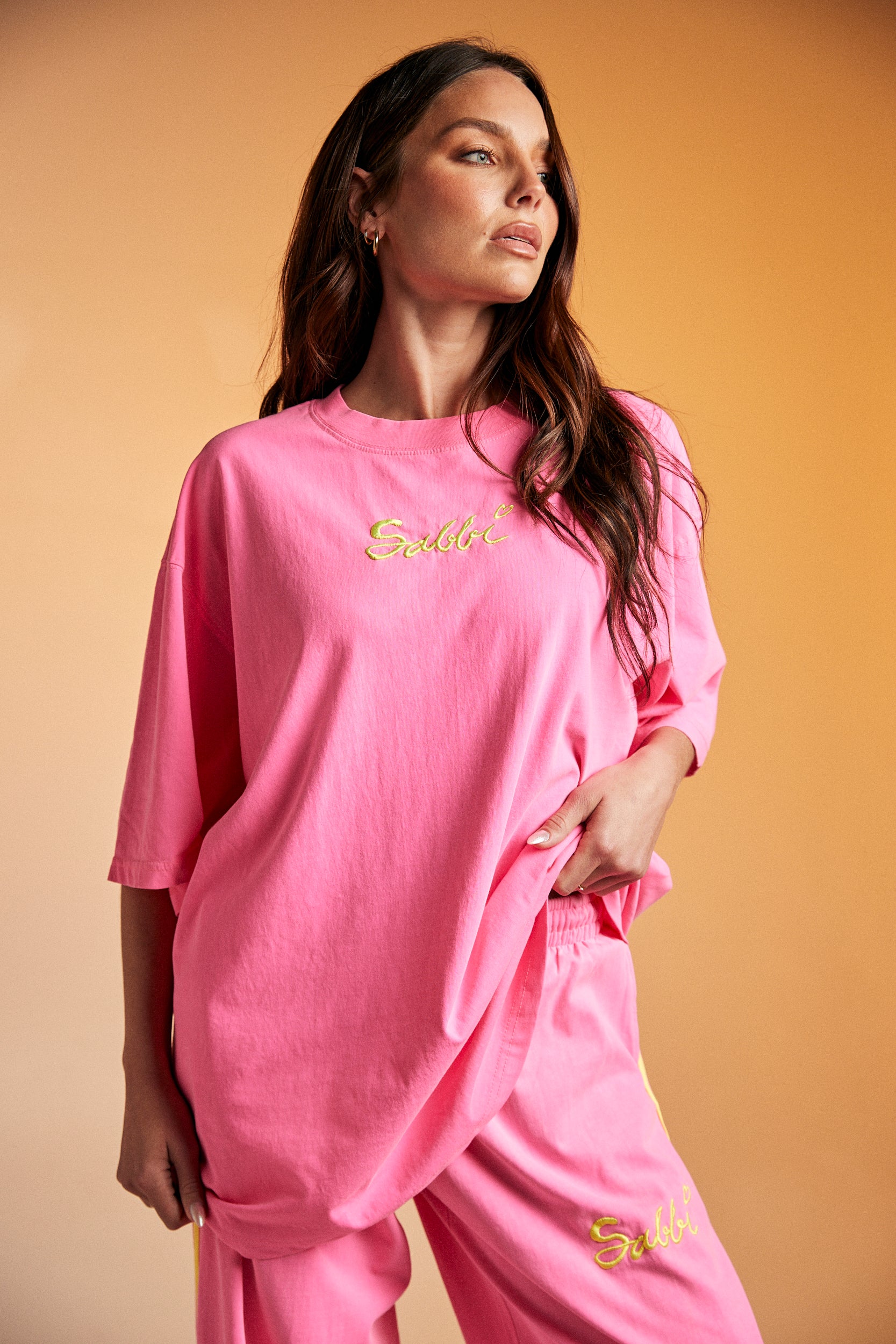 Get ready to steal the spotlight in The Stand Out Tee - Fluro Pink — a bold, feel-good statement piece that’s made to brighten your day (and everyone else’s).

Crafted from premium cotton, this oversized tee features a vibrant fluro pink base with aqua contrast trims for that perfect pop of contrast. The front showcases an eye-catching festival-inspired graphic, while the back brings the good vibes with Sabbi’s signature artwork and an empowering message: “Be You. Be Bold. Be Bright. Be the Whole Rainbow.”