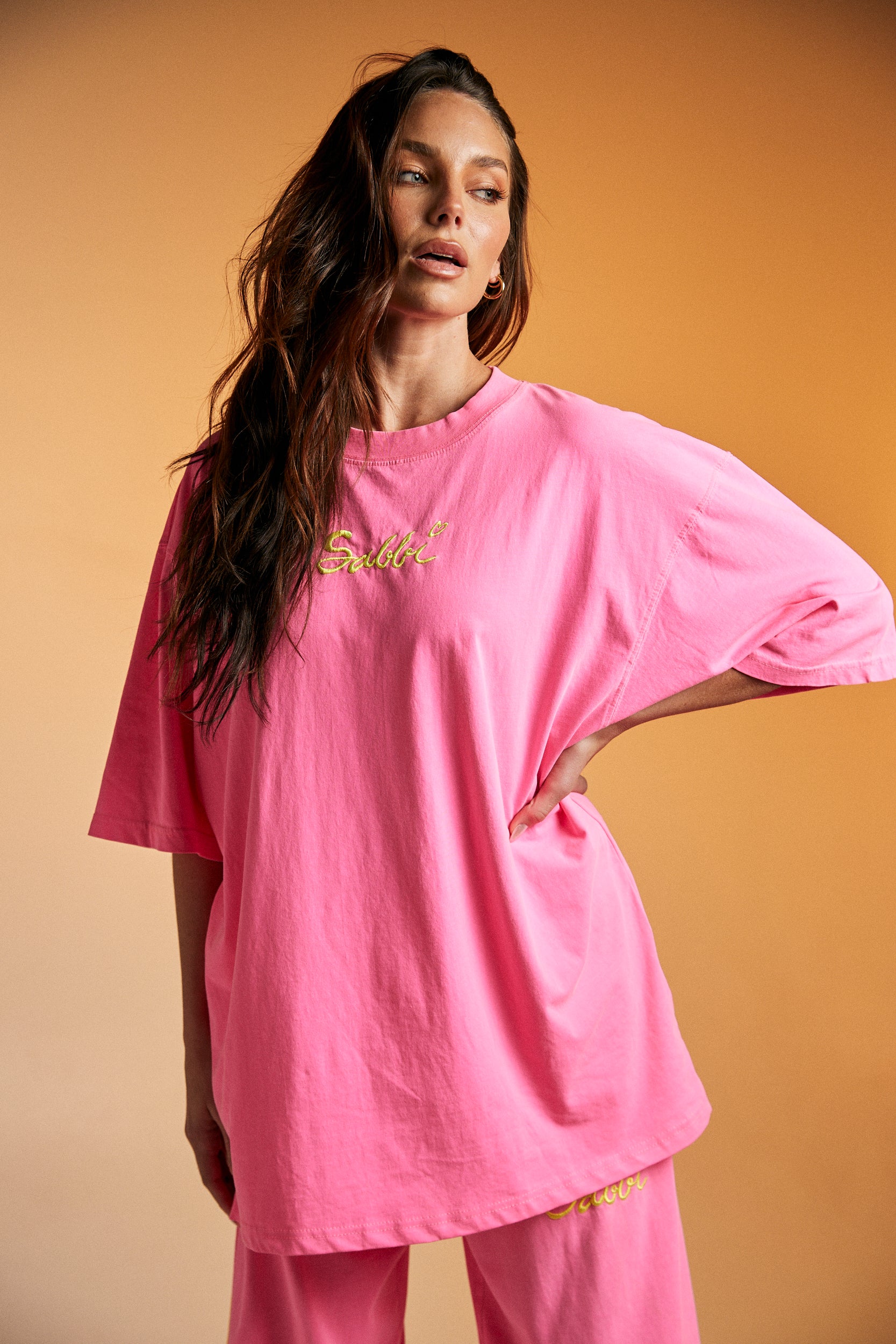 Get ready to steal the spotlight in The Stand Out Tee - Fluro Pink — a bold, feel-good statement piece that’s made to brighten your day (and everyone else’s).

Crafted from premium cotton, this oversized tee features a vibrant fluro pink base with aqua contrast trims for that perfect pop of contrast. The front showcases an eye-catching festival-inspired graphic, while the back brings the good vibes with Sabbi’s signature artwork and an empowering message: “Be You. Be Bold. Be Bright. Be the Whole Rainbow.”