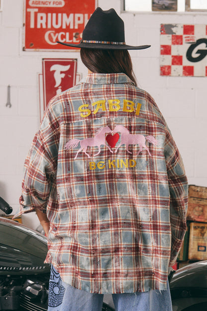 The Horse Power Distressed Flannel Shirt – Burgundy

Where grit meets kindness. The Horse Power Distressed Flannel in Burgundy is your go-to layer for laid-back rebellion. With a sun-faded, vintage-inspired burgundy and blue check, this oversized shirt brings serious attitude with a soft side.

The back steals the show with SABBI’s signature embroidered pink ponies, chenille red heart, and “BE KIND” slogan — a sweet reminder stitched into a tough-as-nails piece. The right sleeve is embroidered with “HORSE P