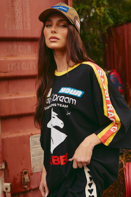 Make a bold statement and embrace laid-back comfort with The Very Oversized Don't Quit Your Day Dream Tee. This racing-inspired piece takes vintage moto vibes and gives them a modern streetwear twist. Featuring a relaxed, ultra-oversized fit, it’s perfect for throwing on and making your outfit look effortlessly cool.

Crafted from premium, soft-touch cotton, it showcases striking front graphics with the iconic Sabbi double horse logo, sleeve branding, and vibrant racing stripes. The back design turns heads 