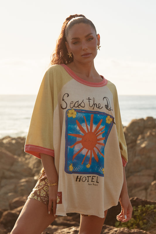 Sabbi - Easy, breezy, and made for chasing golden hour. The&nbsp;Seas the Day Raglan Tee is your throw-on-and-go staple, designed with a relaxed oversized fit and soft raglan sleeves for that perfectly worn-in feel. Featuring the hand-drawn Seas the Day Hotel graphic front and centre, this tee captures carefree coastal energy with a nostalgic, sun-faded vibe.