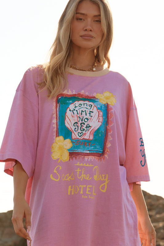 Sabbi - Meet your new off-duty essential. The Seas The Day Hotel Tee – Pink is all about laid-back beach energy with a playful, feel-good twist. Washed in a sun-faded pink and finished with hand-drawn coastal artwork, this oversized tee brings vintage surf nostalgia straight into your everyday wardrobe.