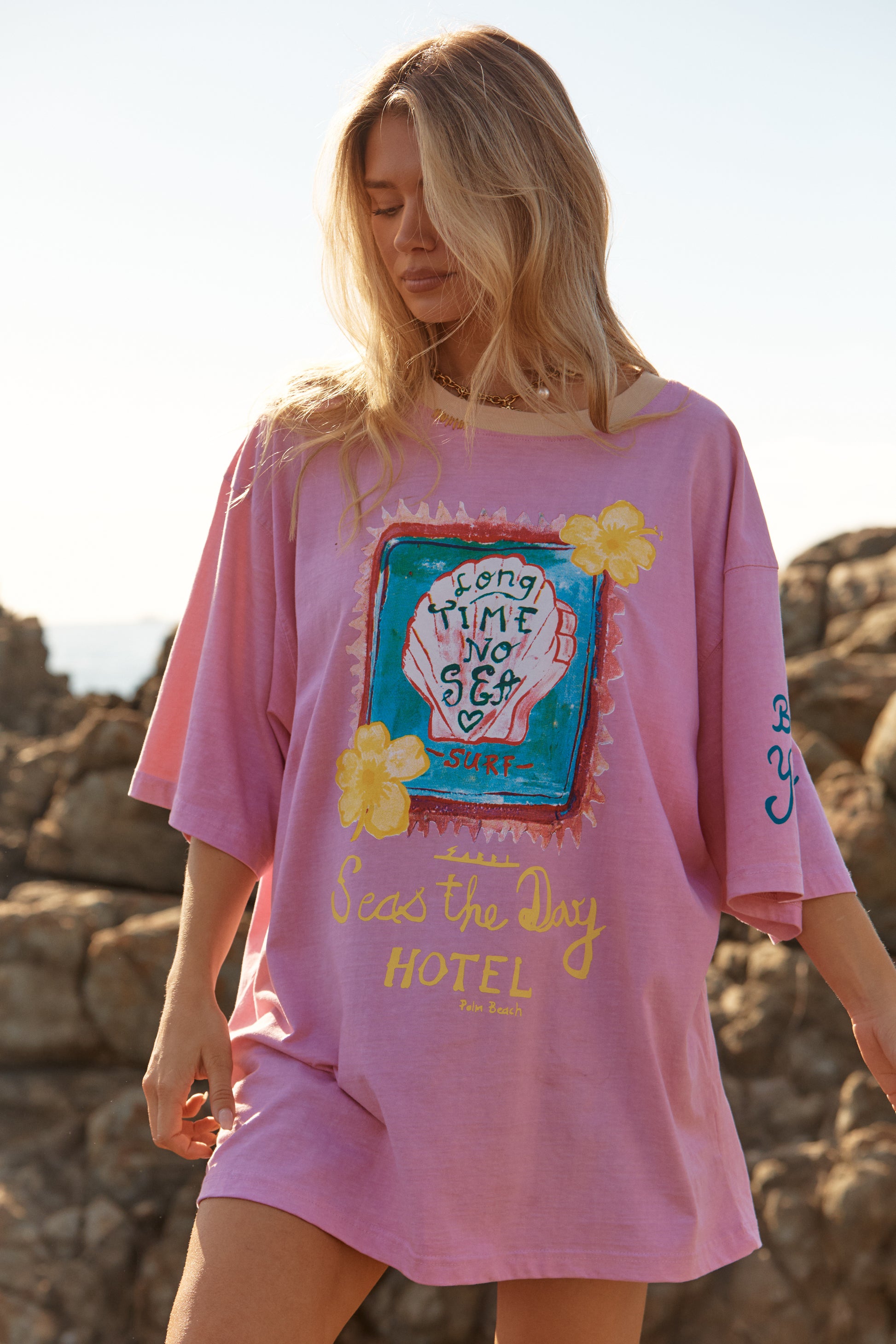 Sabbi - Meet your new off-duty essential. The Seas The Day Hotel Tee – Pink is all about laid-back beach energy with a playful, feel-good twist. Washed in a sun-faded pink and finished with hand-drawn coastal artwork, this oversized tee brings vintage surf nostalgia straight into your everyday wardrobe.