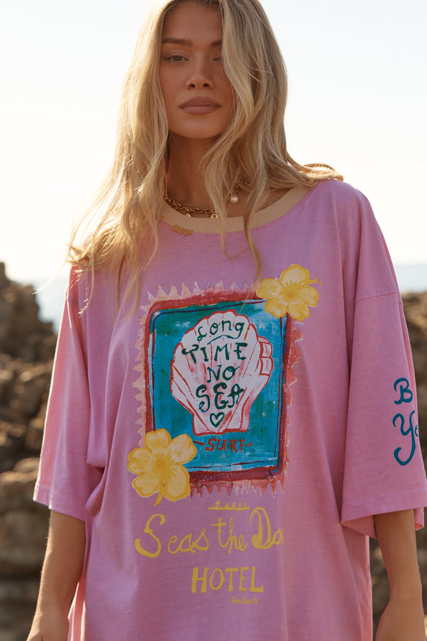 Sabbi - Meet your new off-duty essential. The Seas The Day Hotel Tee – Pink is all about laid-back beach energy with a playful, feel-good twist. Washed in a sun-faded pink and finished with hand-drawn coastal artwork, this oversized tee brings vintage surf nostalgia straight into your everyday wardrobe.