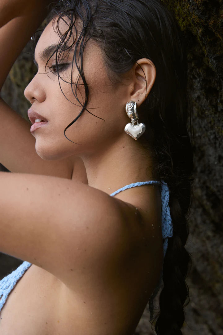 Timeless with a modern edge, the Elena Earrings in silver are a heart-shaped ode to the sunlit serenity of the Mediterranean. Crafted in radiant silver with hand-set freshwater pearls and pearlescent enamel detailing, they reflect the soft glow of sea and sky with every turn.