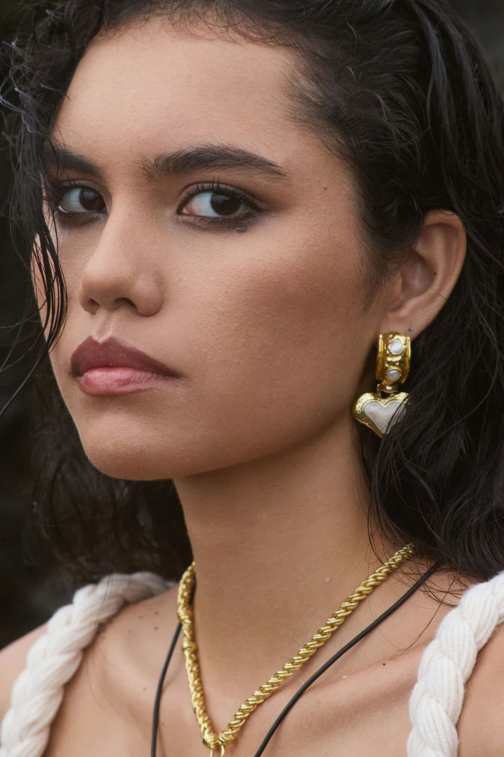 The&nbsp;Elena Earrings are a romantic nod to sun-soaked summers and ancient beauty,&nbsp;where antique ruins meet modern elegance. Featuring heart-shaped silhouettes bathed in gold, adorned with lustrous freshwater pearls and hand applied pearlescent enamel detailing.



Part of our Sirens Collection, these earrings draw from the timeless charm of the Mediterranean—where molten textures echo the ruins of antiquity, and every shimmer captures the glint of sea and sky. 