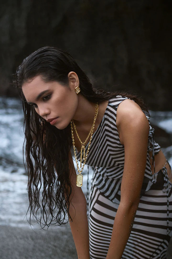 Playful yet powerful, the Cassia Necklace is a bold expression of modern mythology. Designed in a lariat style with a textured, rope-like gold chain, this statement piece features three symbolic charms—star, heart, and dog tag—each suspended at asymmetrical lengths and detailed with pearl enamel accents.