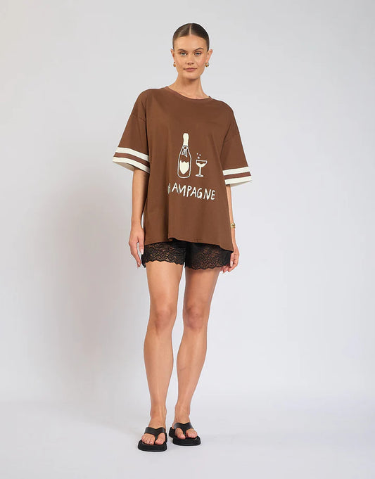 Casual comfort meets effortless style with The Champagne Tee — a versatile wardrobe essential designed for everyday wear.

Crafted on a warm brown base, this tee features subtle ribbing on the sleeves for a touch of texture and shape, while the bold front print adds personality and edge. The relaxed fit makes it easy to style with denim, skirts, or shorts, giving you an elevated casual look that works day or night.
