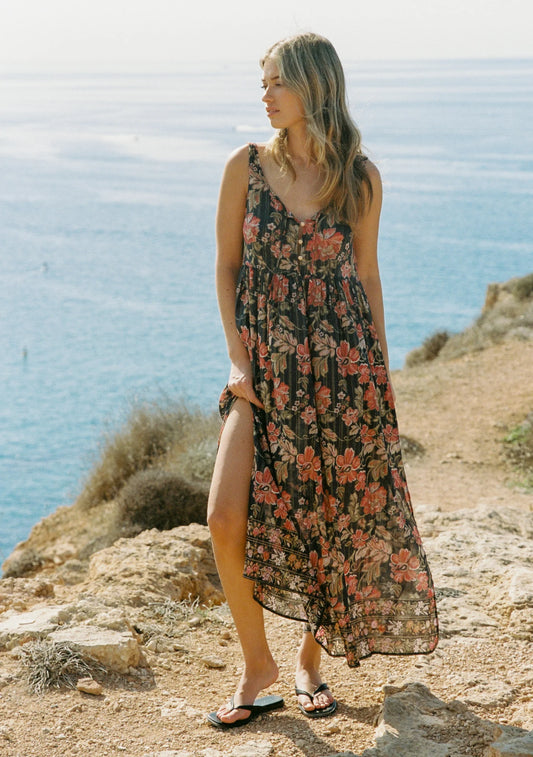 The Beachside Maxi Dress, an all-time Auguste best-seller for a reason, returns in the black-based Vesper Floral with striking border print detail. Designed with a round neckline, specialty gold button-front closure, and a neck tie finished with bead ends for a delicate touch. With a relaxed fit that falls to a floaty hem and side splits for added movement, this shimmering maxi is crafted from our trademark cotton with gold lurex thread woven throughout. A timeless silhouette reimagined, it’s the summer sta