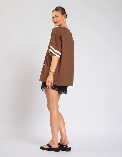 Casual comfort meets effortless style with The Champagne Tee — a versatile wardrobe essential designed for everyday wear.

Crafted on a warm brown base, this tee features subtle ribbing on the sleeves for a touch of texture and shape, while the bold front print adds personality and edge. The relaxed fit makes it easy to style with denim, skirts, or shorts, giving you an elevated casual look that works day or night.