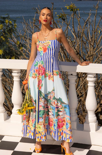 The Positano Sundress in Blue captures the spirit of summer in every stitch. With its picturesque coastal print, adjustable straps, and shirred back panel for a flattering fit, this dress blends comfort and sophistication effortlessly. The soft, lightweight linen-blend fabric flows beautifully, making it ideal for sunny days, weekend escapes, and long lunches by the sea. Finished with a chic exposed gold back zipper and cotton lining, it’s your go-to statement sundress of the season.