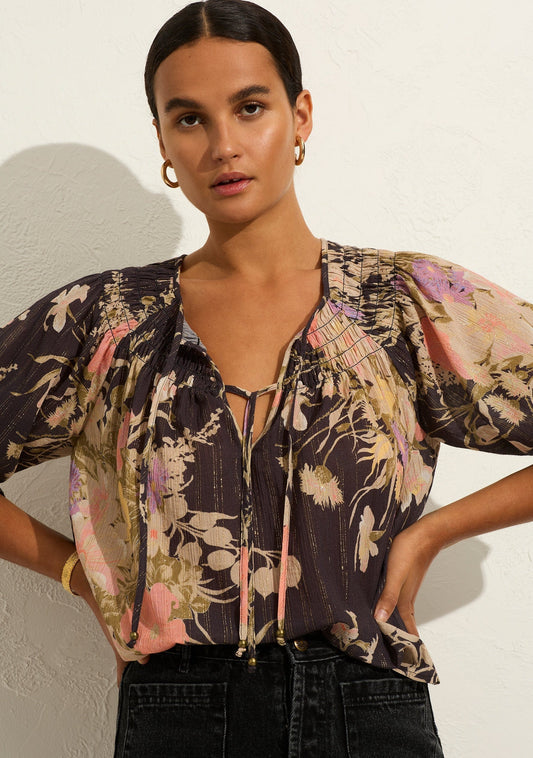 The Brielle Blouse in vintage-inspired Celestia print, with trademark gold lurex thread, showcases a V neckline with an optional tie, shirring at the neckline, and raglan puff sleeves.