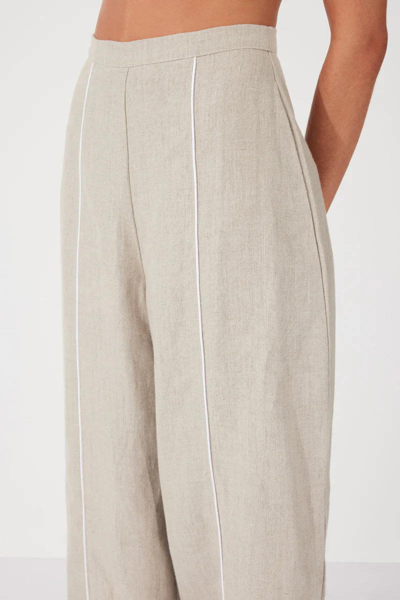 The Husk Contrast Linen Pant by Zulu & Zephyr is effortlessly wearable, to be dressed up or down, featuring a high fixed waistband with back zip closure, a loose tailored leg, and contrast piping detailing.