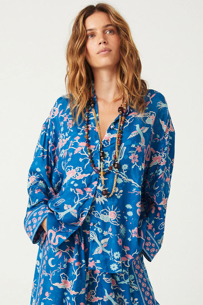 The Desert Bandita Shirt in Cobalt is a statement piece that combines comfort with style. Made from soft, silk-like Jacquard woven fabric adorned with captivating desert motifs in vivid hues, this shirt offers a relaxed yet polished look. Its versatile design allows it to be dressed up or down, making it an essential addition to your wardrobe. Wear it with the matching Desert Bandita Wide Leg Pant for a striking ensemble or pair it with your favourite denim for a chic, casual vibe.