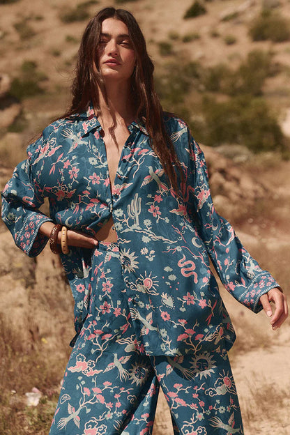 The Desert Bandita Shirt in Cobalt is a statement piece that combines comfort with style. Made from soft, silk-like Jacquard woven fabric adorned with captivating desert motifs in vivid hues, this shirt offers a relaxed yet polished look. Its versatile design allows it to be dressed up or down, making it an essential addition to your wardrobe. Wear it with the matching Desert Bandita Wide Leg Pant for a striking ensemble or pair it with your favourite denim for a chic, casual vibe.